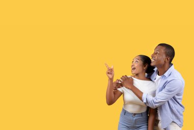 Heyecanlı siyah çift, sarı stüdyo arka planında izole edilmiş güzel metin ya da reklam için fotokopi çekiyorlar, kadın ve erkek harika bir teklif sunuyorlar.