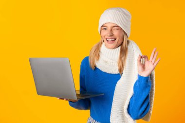 Mavi kazaklı mutlu kadın dizüstü bilgisayar tutuyor, eliyle 