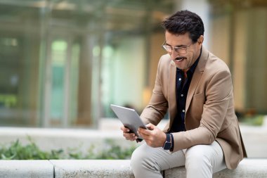 Açık havada dijital tablet kullanan, resmi takım elbiseli, olgun bir adam. Orta yaşlı işadamı iş toplantısından önce bloknotlarda sohbet ediyor, e-posta ya da iş telefonu uygulamalarını kontrol ediyor, boşluğu kopyalıyor