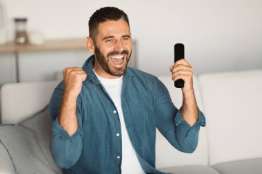 Orta yaşlı bir adam TV 'de futbol maçı izlerken sevinçten havalara uçuyordu. Spor taraftarı zaferi kutluyor. Uzaktan kumandayla evet işareti yapıyor.