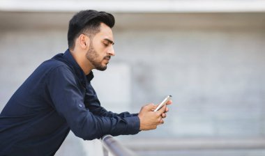 Endişeli Arap işadamı şehrin arka planında akıllı telefondan kayıyor, sorunlarla ve dijital ikilemlerle karşı karşıya, olumsuz mesajlar ve iş haberleri okuyor. Boşluğu kopyala