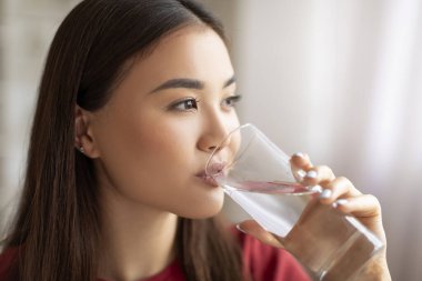Sağlıklı sıvı. Evinde bardaktan su içen güzel Asyalı kadın, Cilt tazeleyici içeceği, seçici bir odak noktası ve boş alanı olan susuz Koreli genç bayan portresi.