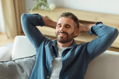 Dinlenme Konsepti. Modern Oturma Odası İçi 'nde rahat koltukta oturan mutlu orta yaşlı adam. Neşeli, rahat, gevşeyen, arkana yaslanan hafta sonunun ve boş zamanın tadını çıkaran adam.