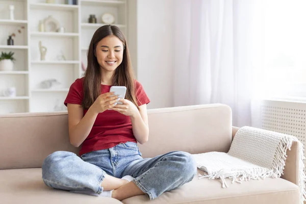 Souriant Jeune Femme Asiatique Avec Smartphone Détendre Sur Canapé Maison — Photo
