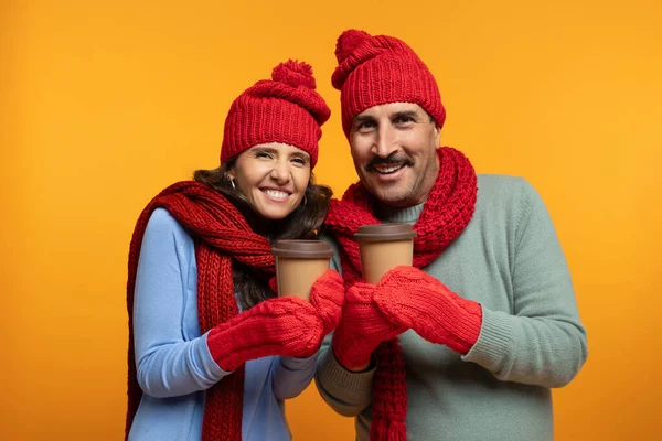快乐的资深欧洲裔丈夫和妻子戴着帽子 喝着热饮 在冬天热身 隔离在橙色工作室的背景下 广告和优惠 咖啡和茶外卖 — 图库照片