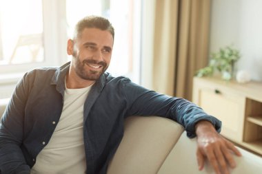 Orta yaşlı bir adam, rahat bir şekilde kanepeye uzanmış, rahat, rahat bir oturma odasında, rahat ve neşeli bir ev hayatı yaşıyor. Mutlu ev sahibinin fotoğrafı.
