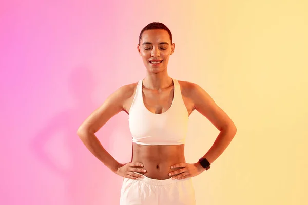 Cheerful slim young latina lady athlete in sportswear with close eyes, rest on neon pink studio background. Break from sports, body care, weight loss and fit lifestyle motivation