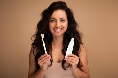 Gülümseyen esmer, uzun saçlı, bin yıllık kadın elinde ahşap ya da bambu organik, çevre dostu diş fırçası ve diş macunu tutuyordu. Mükemmel dişlerini bej arka planda gösteriyordu. Diş sağlığı konsepti