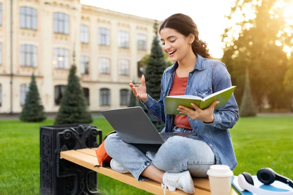 Online education, webinar, course. Happy beautiful young indian woman student have online class while chilling at park, using laptop, pass online exam, video call with tutor, copy space