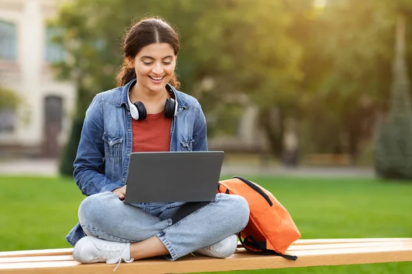笑顔のインドの若い女性学生は ラップトップで作業するベンチに座って 大学のキャンパスで休んで 屋外の試験のために準備しました テクノロジー リモートワーキングコンセプト コピースペース — ストック写真