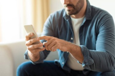 Sıradan giyinmiş, akıllı telefon aleti kullanan, web sörfü yapan ve kapalı alanda mesajlaşan tanınmamış orta yaşlı bir adam. Telefon ekranına dokunan adamın görüntüsü. Mobil iletişim konsepti