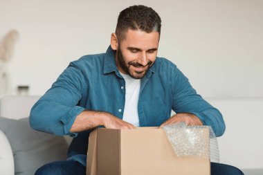 Mutlu alıcı. Gülümseyen orta yaşlı bir adam, evdeki modern oturma odasındaki koltukta otururken, başarılı alışverişlerden sonra kutuları açarak teslimat yapıyordu. Perakende ve tüketim