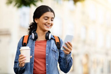 Zeki telefonlu neşeli genç Hintli öğrenci ve çalışma kitapları dışarıda duruyor, üniversiteden sonra şehirde yürüyen mutlu doğu kadını, telefona bakıyor ve gülümsüyor, uzay kopyaları kopyalıyor.
