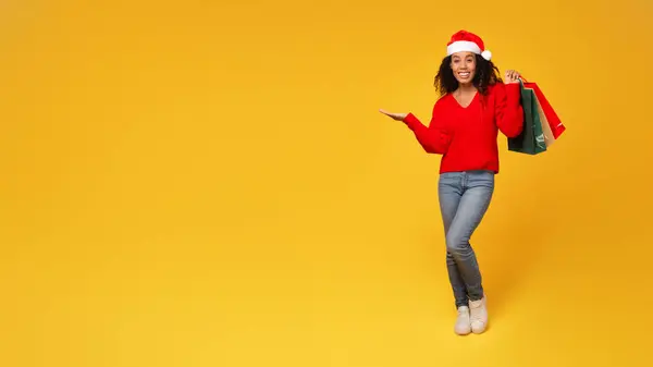 Enthusiastic Black Lady Santa Hat Gripping Shopping Bags Hand Pointing — Stock Photo, Image