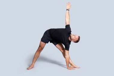 Sakallı, spor giyim yogası, nefes egzersizleri, esneme hareketleri, gri stüdyo arka planında izole edilmiş, uzun boylu yakışıklı Avrupalı bir adam. Spor ve denge