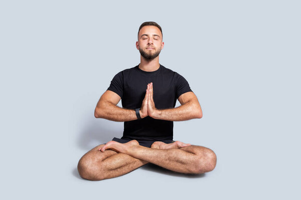 Calm young caucasian man with beard in sportswear practice yoga in lotus position, enjoy breath exercises, peace, isolated on gray studio background, full length. Workout and health care
