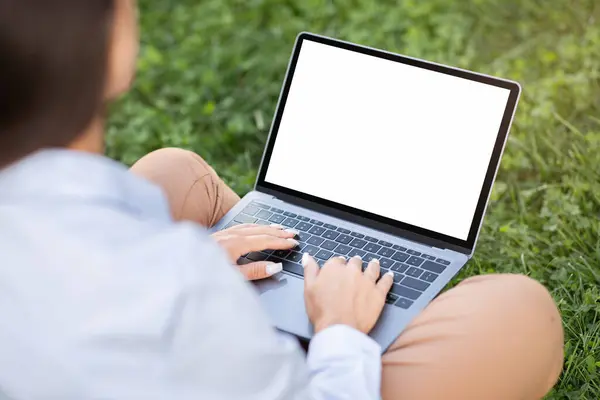Young caucasian woman enjoy work, typing on laptop with empty screen, sit on grass in city park, outdoors, cropped. Business lifestyle, study, digital nomad, project startup