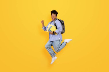 Coşkulu siyahi öğrenci sevinçten havalara uçuyor, not defterlerini tutuyor ve sırt çantası takıyor, parlak sarı arka planda eğitim başarısını simgeliyor.