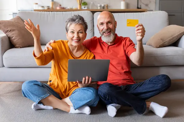 E-banking Concept. Excited Senior Spouses With Laptop And Credit Card Posing In Home Interior, Happy Elderly Couple Enjoying Online Payments And Easy Money Transfers, Smiling At Camera