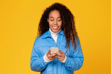 Neşeli genç siyahi bayan cep telefonuyla meşgul, parlak sarı arka plana gülümsüyor, kaygısız tatil havasını somutlaştırıyor.