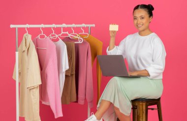 Online Alışveriş Sitesi. İnternet alışverişleri için dizüstü bilgisayar ve kredi kartı kullanan mutlu Asyalı kadın, Pembe Stüdyo Arkaplanının Üzerinde Gülümseyen Alışveriş Kadını Poz Veren,