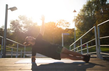 Ahşap iskelede antrenman yaparken kenar tahtası egzersizi yapan genç sporcu. Spor kıyafetli atletik adam güneşli yaz gününde spor salonunda dayanıklılık egzersizi yapıyor. Etkin Yaşam Biçimi