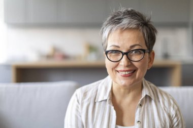 Evdeki koltukta oturan güzel, gülümseyen yaşlı bir kadının portresi, gözlükleriyle kameraya bakan mutlu, yaşlı bir kadının oturma odasındaki koltukta dinlenmesi, boş alan.