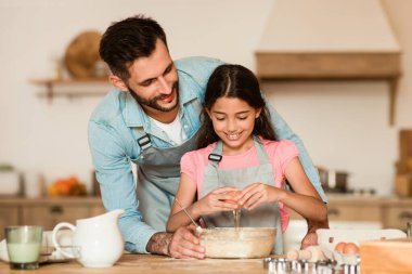Neşeli baba, güler yüzlü kızına güler yüzlü mutfakta pişirmek için hamuru karıştırırken aile bağı ve aşçılık eğitimi sahnesi yaratırken rehberlik ediyor.