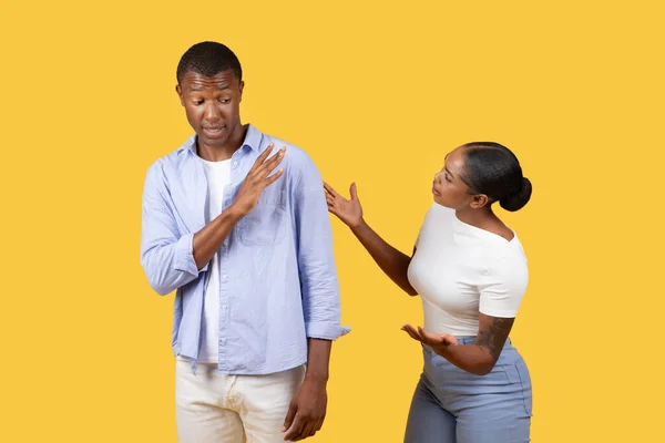 Frustrated black woman is shouting at man who appears dismissive, showing common social conflict scenario against bright yellow background