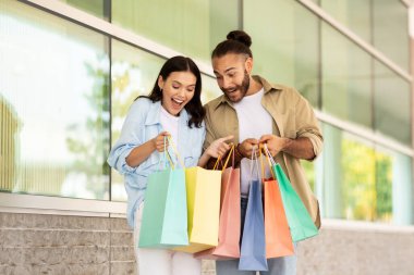 Glad surprised millennial caucasian couple shopaholics look at many packages, enjoy shopping together, new clothes order in mall. Lifestyle, sale and relationships, ad and offer, discount clipart