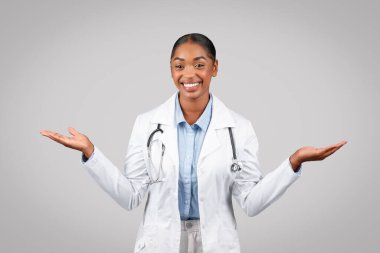 Neşeli bin yıllık siyahi kadın doktor ellerinde fotokopi alanı, kollarını açarak gri arka planda, stüdyoda izole bir şekilde duruyor. Sağlık hizmeti tavsiyesi, seçim, reklam ve teklif, tıbbi yardım