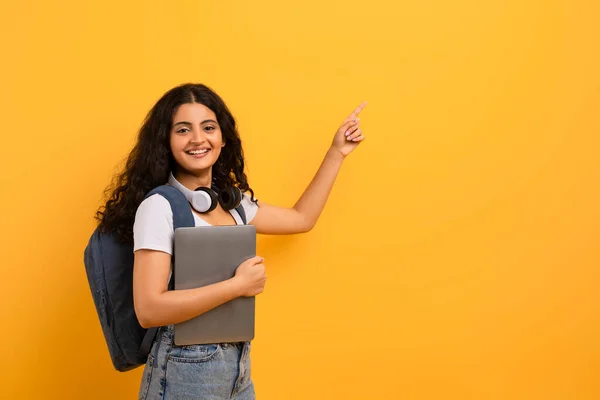 リモート教育の機会 彼女の手にバックパックとラップトップでカジュアルな服を着て 陽気でかわいい若いインドの女性学生 コピースペースを指して 黄色の背景 パノラマ — ストック写真