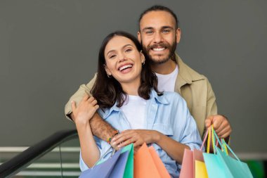 Bin yıllık beyaz erkek alışveriş meraklısı bir sürü paketle karısına sarılıyor, alışveriş merkezinden birlikte alışveriş yapıyor. Hediyeler ve ilişkiler için satış, satın alma ve alıcı duyguları, yaşam tarzı