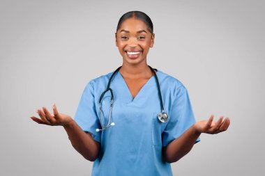 Milenyum siyahi doktor cerrahı, mavi üniformalı hemşire, el ele tutuşmuş, elleri boş, gri stüdyo arka planında izole edilmiş. Tıbbi reklam, teklif, profesyonel seçim.