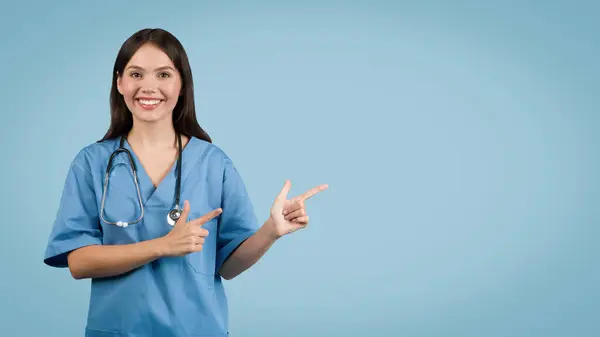 Впевнена Жіноча Медсестра Блакитній Формі Вказує Бік Обома Руками Посміхаючись — стокове фото