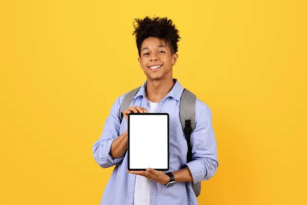 年轻快乐的黑人学生 背负盈亏 带着空白屏幕展示数码平板电脑 供教育应用或网站在生机勃勃的黄色背景下进行模仿 — 图库照片
