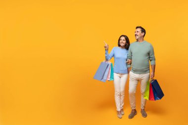 Gülümseyen kıdemli Avrupalı erkek ve bayanın alışveriş torbaları, alışveriş, fotokopi alanındaki işaret parmağı, turuncu stüdyo arka planında izole edilmiş. Reklam ve teklif, dikkat satışı