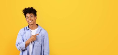 Siyahi adam şık giyinmiş, gülümseyen ve yan tarafı gösteren, metin ya da ürün yerleştirme için boş alan gösteren parlak sarı stüdyo arka planı, panorama