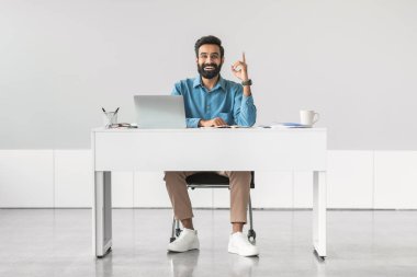 Beyaz masadaki gülümseyen Hintli işadamının fikri, işaret ettiği, dizüstü bilgisayarı ve kahveyle oturduğu, başarılı iş fikrini ya da onayını simgelediği,