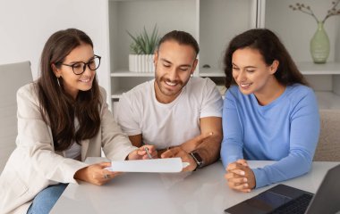Üç farklı profesyonelden oluşan gülümseyen bir ekip. İki kadın ve iki erkek, modern bir ofis masasında bir belgeyle verimli bir takım çalışması yapıyorlar.