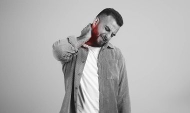 Avrupai sakallı, sakallı, boynuna masaj yapan, acı çeken, kırmızı iltihaplı, gri stüdyo arka planında soyutlanmış, siyah beyaz bir adam. Sağlık sorunları, spazm