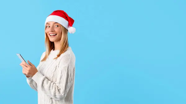 Jovencita Sonriente Sombrero Navidad Navegando Por Teléfono Inteligente Mirando Hacia —  Fotos de Stock