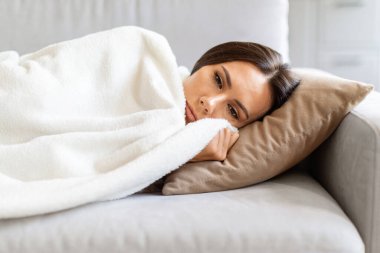 Genç üzgün kadın, yumuşak battaniyeyle kaplı olarak kanepede uzanıyor, üzgün bin yıllık bayan üzgün ve düşünceli görünüyor, mevsimsel depresyondan muzdarip, oturma odasında kanepede dinlenen düşünceli kadın.