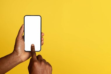 Genç siyahi adamın elleri, sarı stüdyo arka planında izole edilmiş, boş ekranlı cep telefonu kullanıyor, sosyal ağlarda sohbet ediyor. Reklam ve teklif, satılık uygulama, web sitesi tavsiyesi