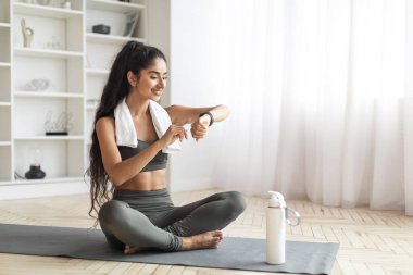 Mutlu genç Hintli kadın antrenman saatini evde kontrol ediyor. Spor, spor, yaşam tarzı, teknoloji ve insan konsepti. Doğu milenyum bayanı kalp atış hızını akıllı saate ayarlıyor, kopyalama alanı