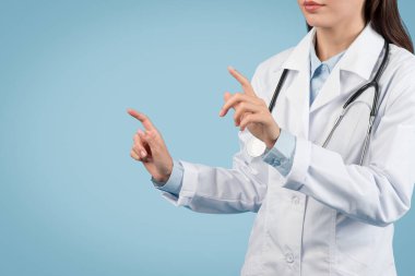 Tıp üniformalı genç Avrupalı bir bayan gelecekteki teknolojiyle etkileşime geçiyor. Görünmez yüksek teknolojili ekrana dokunuyor ve modern tıbbı temsil ediyor.