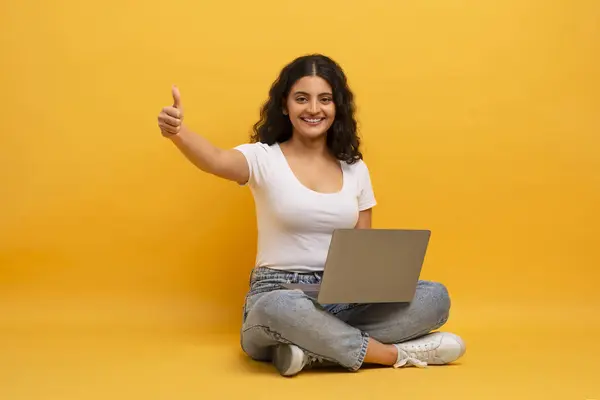 幸せな若いインドの女性 ラップトップのコンピュータのジェスチャーを使用して笑顔をカメラのブラウジングのインターネットは黄色いスタジオの背景の上に座っています 私はフリーランスと距離の仕事の概念が好きです — ストック写真