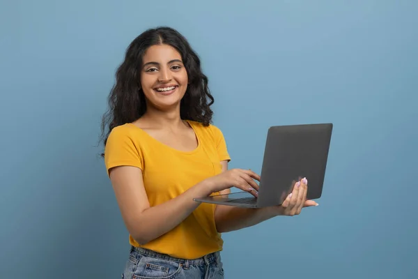 信頼できる若いインド人女性の肖像画は ブルースタジオの背景に隔離されたラップトップコンピュータを使用して 無料のコピースペース Pcで立っている笑顔の女性 カメラを見る — ストック写真