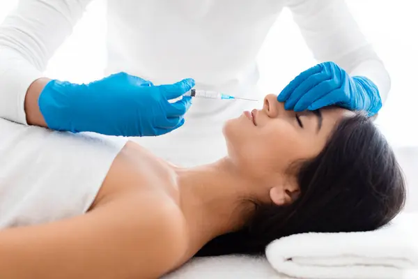 The doctor does injections to correct the hump on the nose with the beauty of young indian woman. The beautician does injections against wrinkles on the face. Womens cosmetology in a beauty salon.