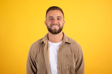 Gülümseyen yakışıklı Avrupalı adam, sarı stüdyo arka planında izole edilmiş, sıradan bir şekilde kameraya bakıyor. Pozitif yaşam tarzı ve insani duygular, reklam ve teklif, çalışma, çalışma
